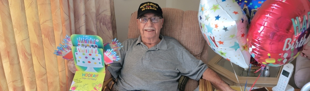 100 Year Old Veteran, William Kansier, sitting in a chair with a card and balloons